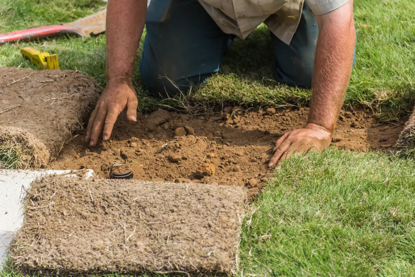 A person in Florida kneels on grass repairing a sprinkler hole, with Palm Beach County, FL tools beside them.