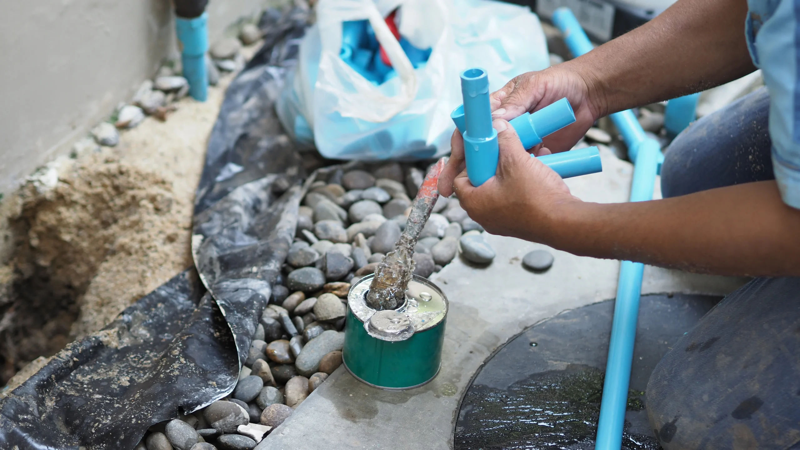 A person in Palm Beach County, FL applies adhesive to a blue PVC pipe for sprinkler installation, tools nearby.