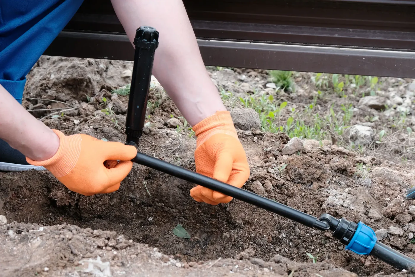 A person in orange gloves installs a black sprinkler pipesprinkler installation in Palm Beach County, FL.