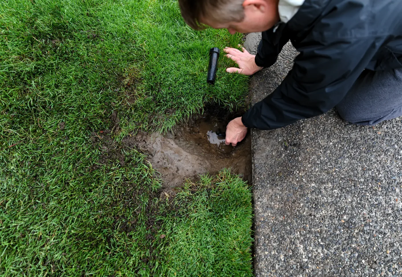 Person kneeling on grass examines water pooling, suggesting sprinkler repair in Palm Beach County, FL may be needed.