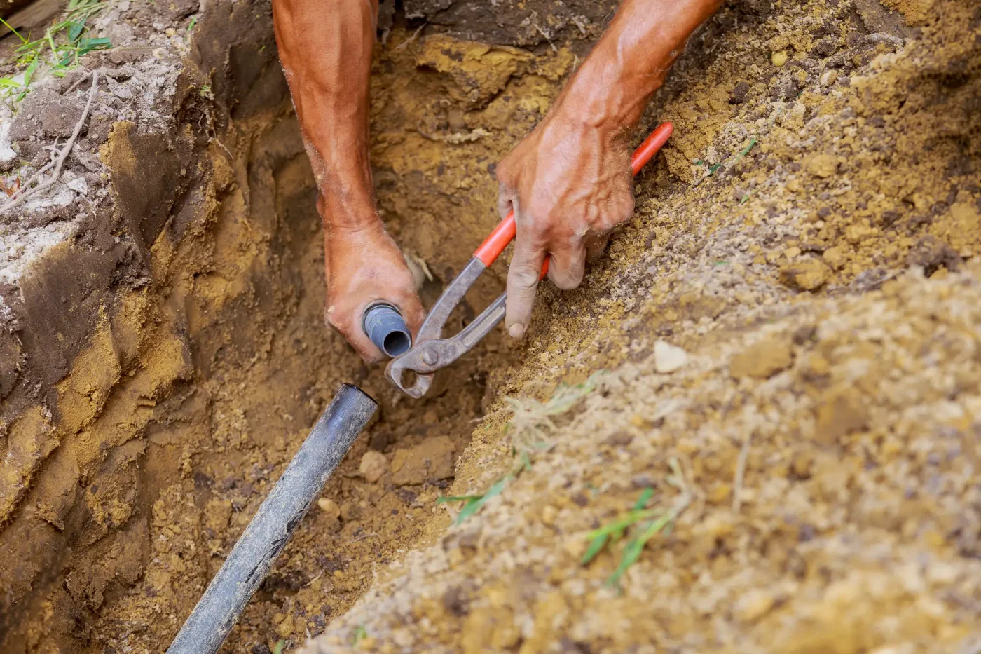 A person connects sprinkler pipes with pliers in a dirt trench during installation in Palm Beach County, FL.