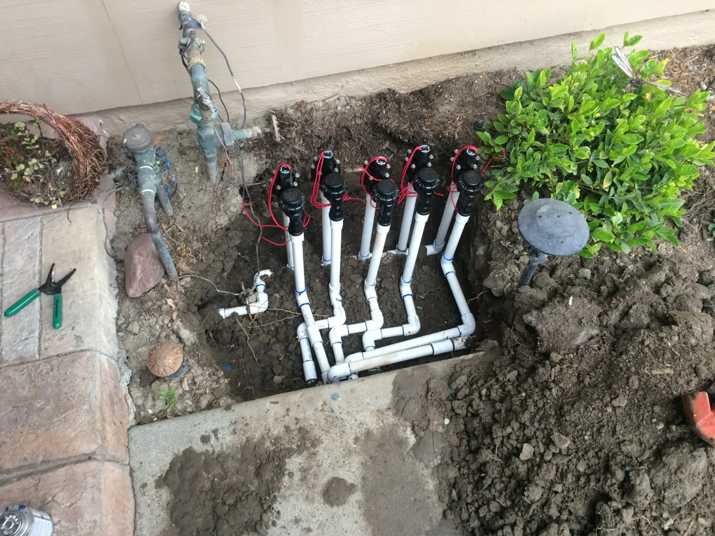 Five sprinkler valves with white PVC pipes for sprinkler repair Palm Beach County, FL sit by a green bush.
