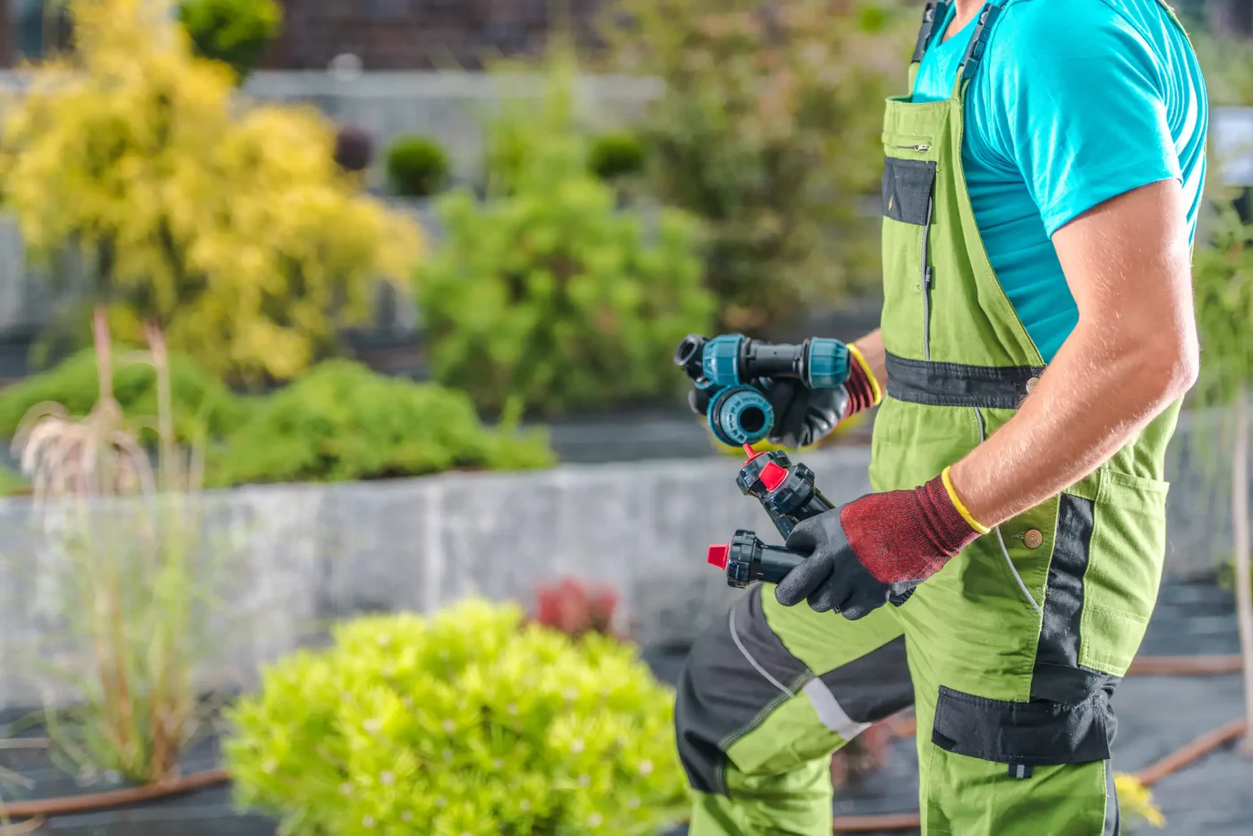 A gardener in green overalls holds sprinkler system parts in a landscaped Palm Beach County, FL garden.
