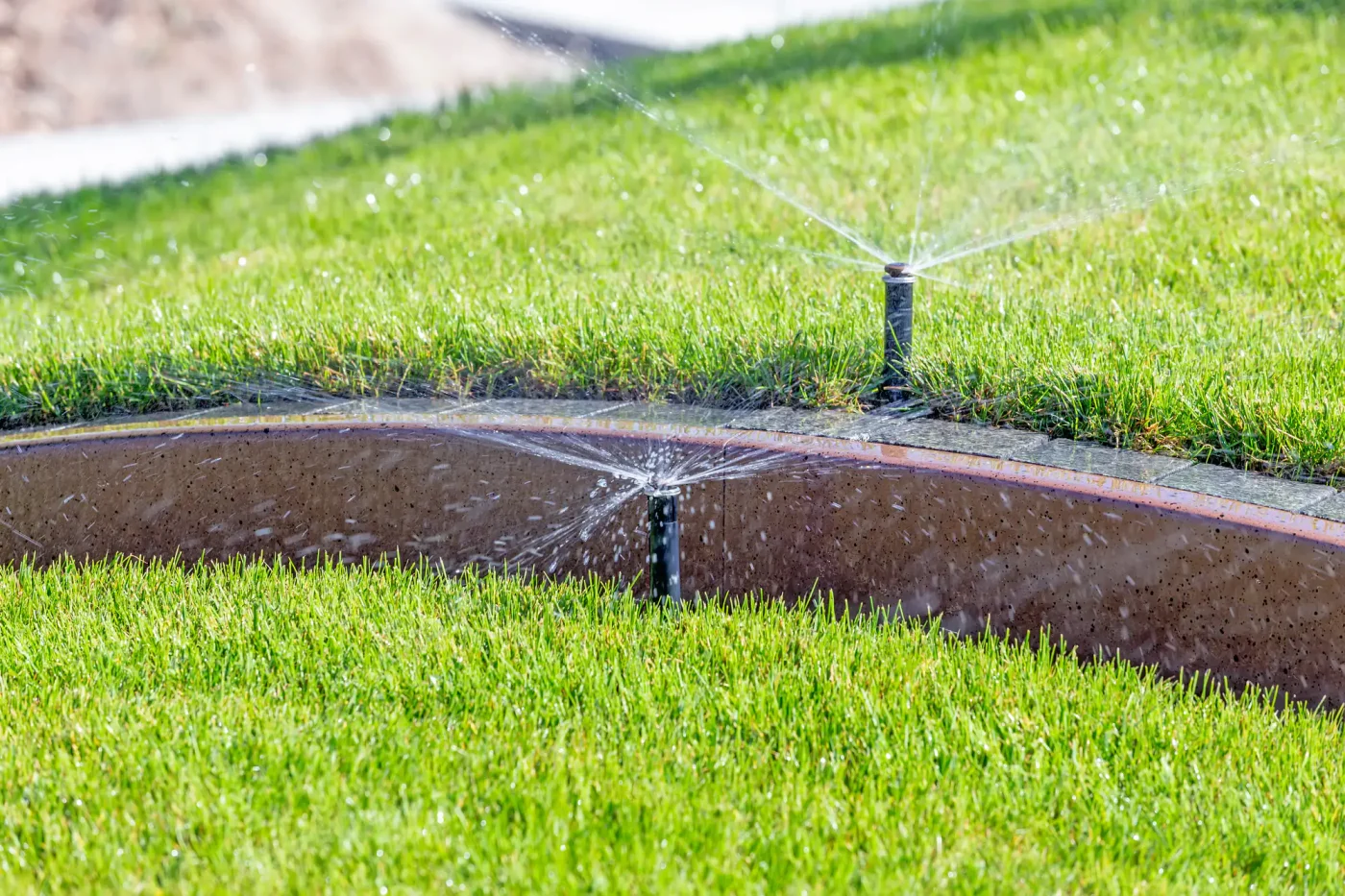 A sprinkler system in Palm Beach County, FL waters bright green grass on a sloped lawn near a concrete border.