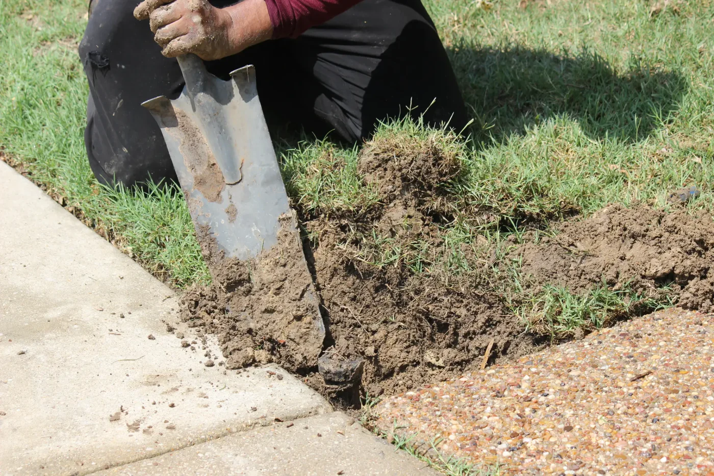 A person edges sod with a shovel along a walkway, preparing for sprinkler repair in Palm Beach County, FL.