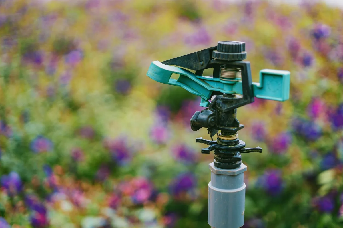 A close-up of a garden sprinkler in action, with flowers behind it and sprinkler systems Palm Beach County, FL.