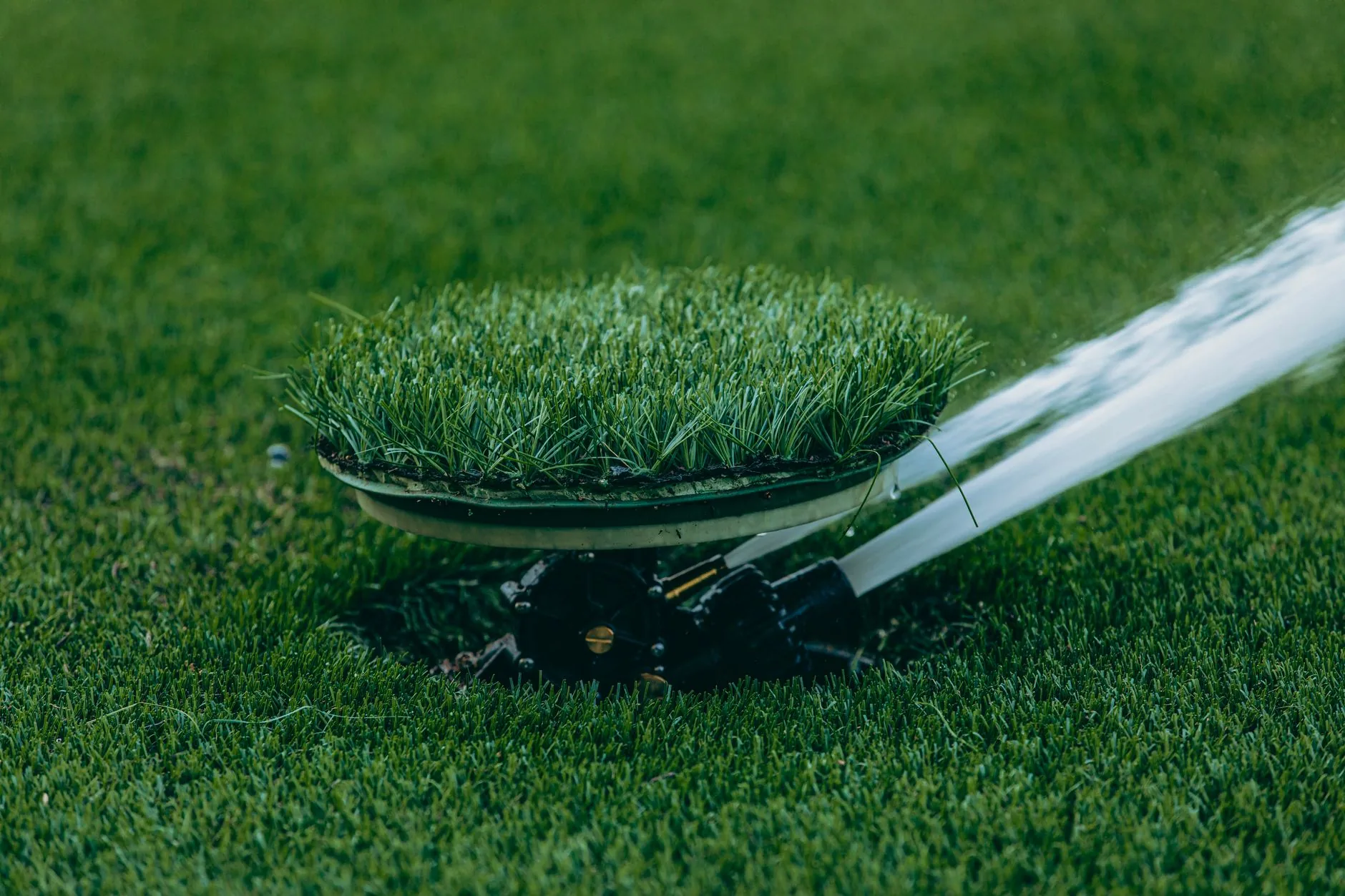 Sprinkler systems Palm Beach County, FL unit sprays water on a lawn, camouflaged with artificial grass.