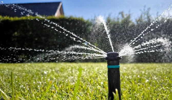 A garden sprinkler installation in Palm Beach County, FL waters vibrant green grass by a house on a sunny day.